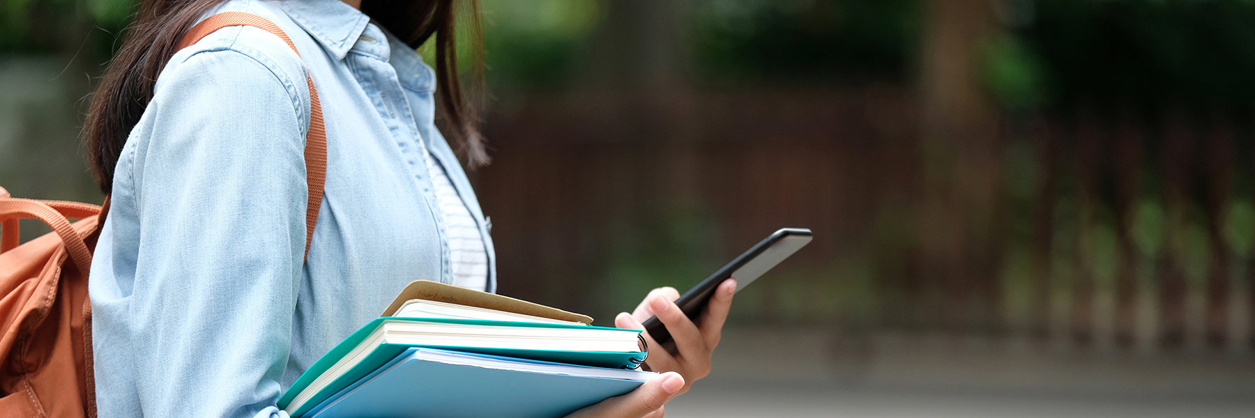 Female student holding books and a cell phone while wearing a backpack