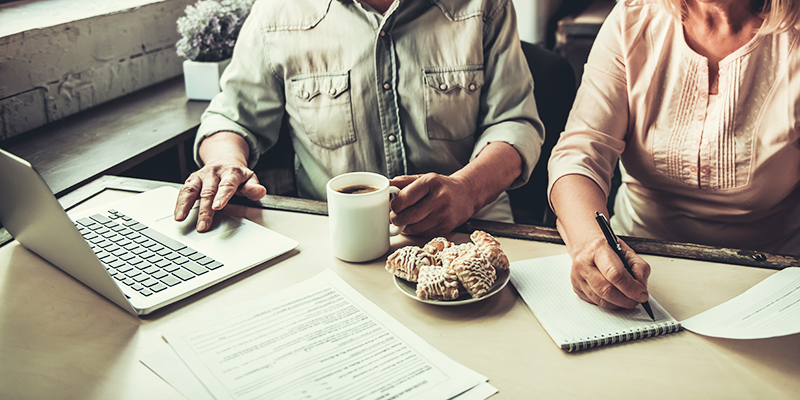 A couple sitting in their kitchen having breakfast and working on a laptop